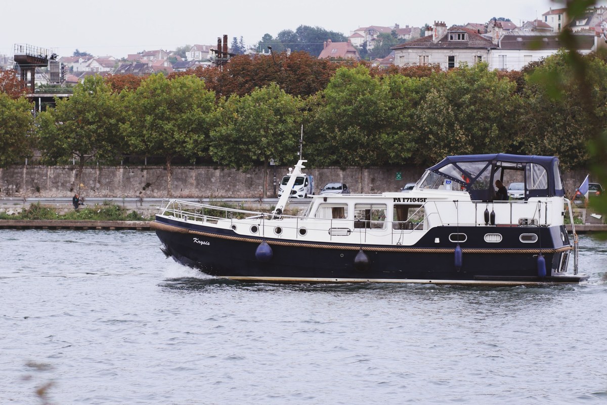 Bateau à moteur avançant sur une rivière bordée d’arbres et de bâtiments